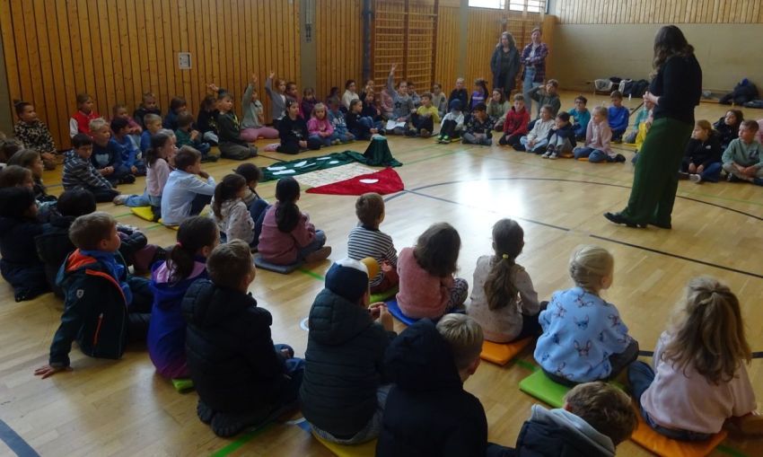 Schüler sitzen in einem großen Kreis auf dem Boden einer Turnhalle