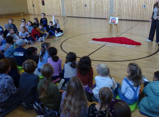 Schulkinder sitzen gemeinsam in der Turnhalle auf dem Boden