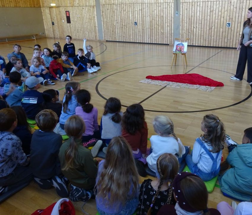 Schulkinder sitzen gemeinsam in der Turnhalle auf dem Boden