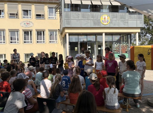 Viele Schüler sitzen auf dem Pausenhof vor einem Schulgebäude