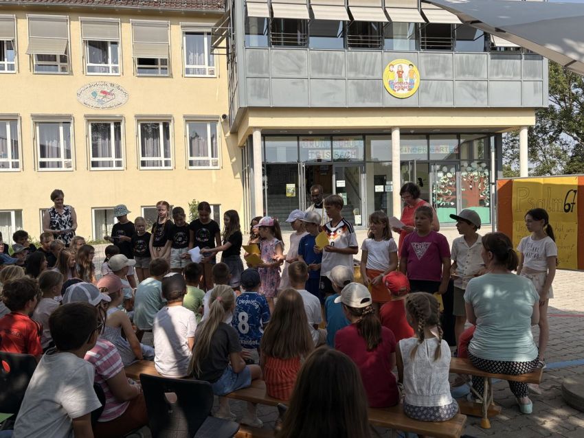 Viele Schüler sitzen auf dem Pausenhof vor einem Schulgebäude