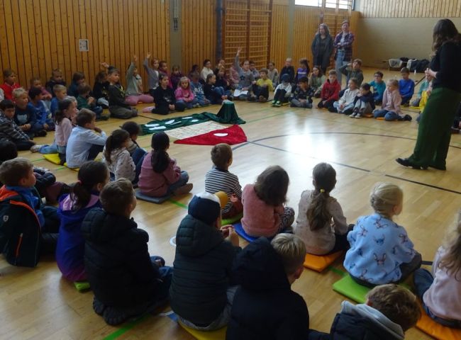 Schüler sitzen in einem großen Kreis auf dem Boden einer Turnhalle